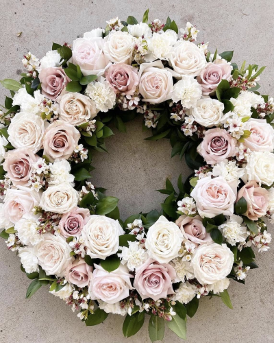 Graceful Remembrance Wreath - The Graceful Remembrance Wreath is a timeless tribute crafted to honor cherished memories with elegance and grace. Composed of soft blush and ivory roses, white carnations, and delicate wax flowers, this circular arrangement is accented with fresh greenery to symbolize eternal love and peace. Ideal for memorials, funerals, or as a heartfelt gesture of sympathy, this wreath conveys comfort and enduring affection in a beautifully classic form.