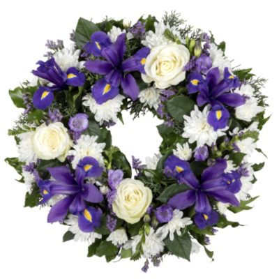 Twilight Tribute Wreath - A stunning and dignified floral wreath featuring rich violet irises, creamy white roses, delicate chrysanthemums, and sprigs of lavender-toned statice. Accented with fresh greenery, this arrangement evokes a sense of serenity and reflection. The deep purples and whites symbolize respect, remembrance, and peace, making it a meaningful choice for memorial services, funerals, or honoring a loved one's legacy.
